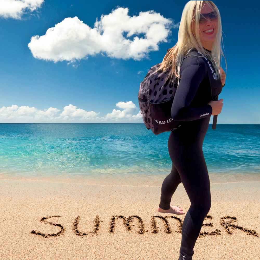 Woman in wetsuit with backpack on beach with 'Summer' written in sand
