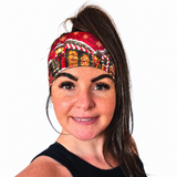Woman with dark hair and a high ponytail wearing a red Christmas festive headband featuring, holiday homes, candy canes and snowy lanterns on a white background
