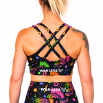 Rear view of a woman wearing a black sports bra and matching high-waisted leggings set by Wild Legs, featuring a vibrant multicolor neon pattern and crisscross back straps.
