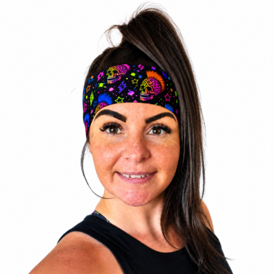 A woman with dark hair in a high ponytail wearing a black headband with a colourful sugar skull and neon pattern, shown against a plain white background.