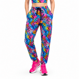 A person modeling bright neon multicolour patterned jogger pants with a matching crop top and pink trainers against a plain white studio background.