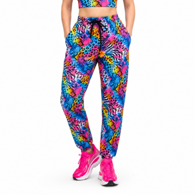 A person modeling bright neon multicolour patterned jogger pants with a matching crop top and pink trainers against a plain white studio background.
