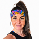 A woman with her hair in a high ponytail wearing a vibrant, multicolored athletic headband with a zebra and leopard print pattern, set against a plain white background.