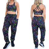 Woman wearing casual pants in black with pastel stars design on a white background, showing front and back of the design.