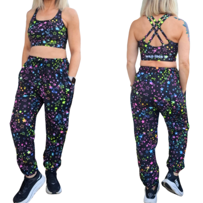 Woman wearing casual pants in black with pastel stars design on a white background, showing front and back of the design.