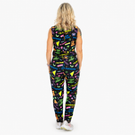 A woman viewed from behind wearing a sleeveless jumpsuit with a colourful retro neon pattern on a black background, set against a plain white studio background.