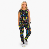 A woman modelling a sleeveless black jumpsuit with a colourful graffiti-style print, paired with white trainers, against a plain white background.