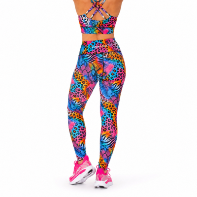 A person shown from the back wearing a matching colourful athletic set with a bright multicolour abstract print, including a sports bra and high-waisted leggings, paired with pink trainers on a white studio background.