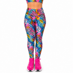 A person wearing bright neon multicolour leggings with an abstract animal-print pattern in pink, blue, yellow, orange, and black, paired with neon pink trainers against a plain white background.