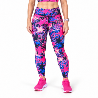 A model wearing high-waisted fitness leggings with a vibrant pink, blue, and black star and splatter pattern, paired with matching pink trainers, shown against a plain white background.