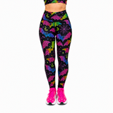 A person wearing high-waisted leggings with a black background and a colourful neon pattern of bats, moons, and stars, paired with bright pink trainers against a plain white background.