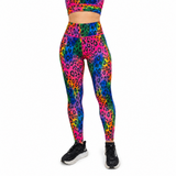 A model wearing high-waisted leggings and a matching sports bra with a vibrant neon rainbow leopard print, paired with black athletic trainers, shown against a plain white background.