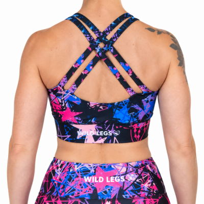 Rear view of a model wearing a sports bra and matching leggings with a vibrant abstract pattern in pink, blue, and black, featuring the brand name 'WILD LEGS' printed on the waistbands.
