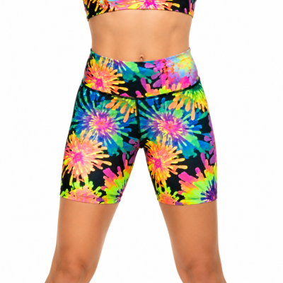 A model wearing high-waisted athletic shorts with a vibrant neon tie-dye burst pattern on a black base, paired with a matching sports bra against a plain white background.