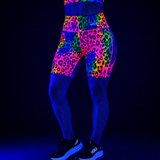 High-waisted athletic leggings with a neon multicolor leopard print pattern, shown on a model under blacklight against a dark background.