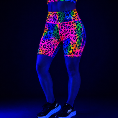 High-waisted athletic leggings with a neon multicolor leopard print pattern, shown on a model under blacklight against a dark background.