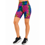 A model wearing high-waisted athletic shorts with a vibrant rainbow neon leopard print, paired with black trainers, shown against a plain white background.