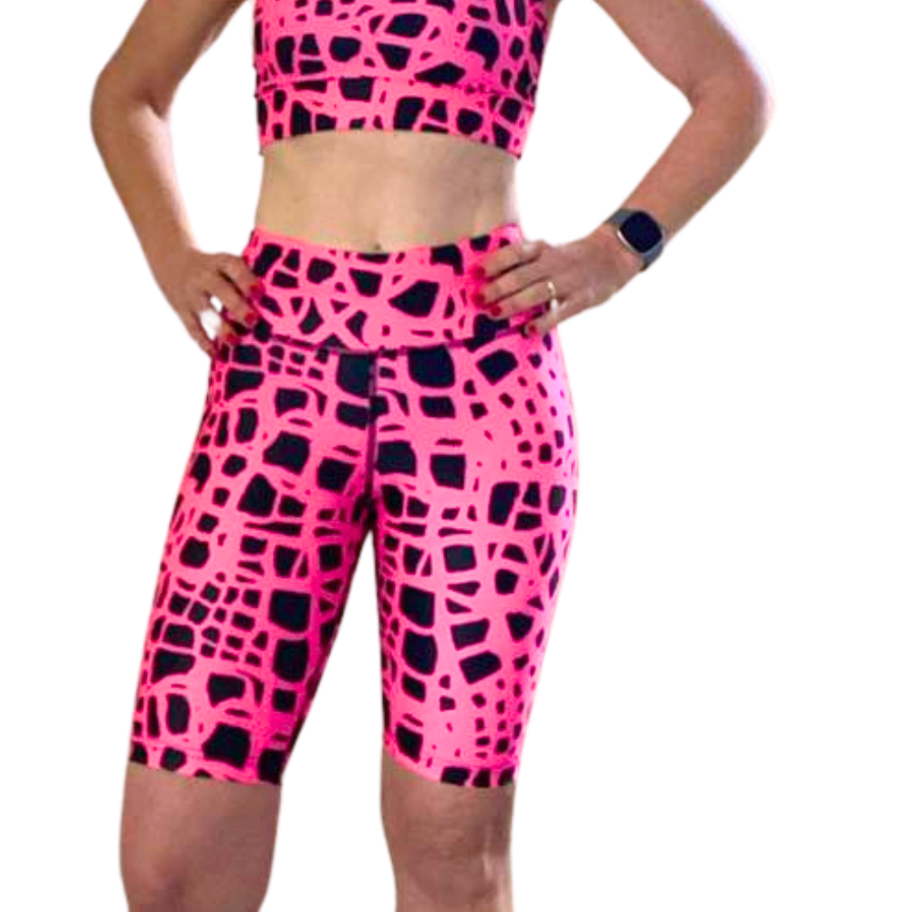Woman wearing pink and black patterned long shorts and crop top on a white background