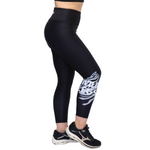 Black high-waisted athletic leggings with a white abstract graphic print on the lower leg, shown on a model from the waist down wearing black Mizuno running shoes against a white background.