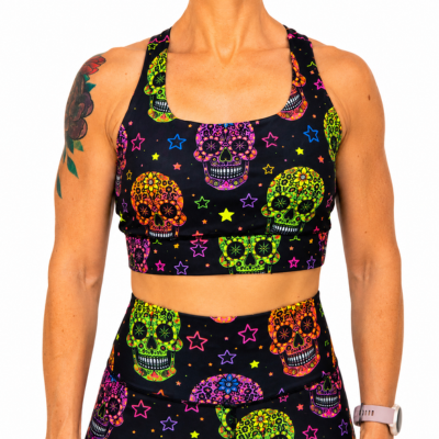 A woman wearing a matching black activewear set with a vibrant, multicolored sugar skull and star print, shown against a plain white background.