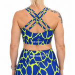 Rear view of a model wearing a matching blue and neon yellow giraffe-print activewear set by Wild Legs, featuring a sports bra with crisscross straps and high-waisted leggings.