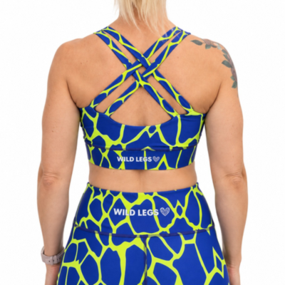 Rear view of a model wearing a matching blue and neon yellow giraffe-print activewear set by Wild Legs, featuring a sports bra with crisscross straps and high-waisted leggings.