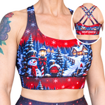 A woman wearing a red and navy Christmas-themed sports bra with a winter village print, featuring an inset circle showing the back straps and the brand name 'WILD LEGS'.