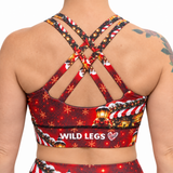 The back view of a sports bra in a Christmas design in red, with gold snow covered lanterns, a Christmas house and the Wild Legs logo on the band, on a white background