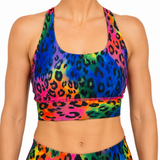 A close-up of a model wearing a vibrant, multicolor leopard print sports bra and matching bottoms against a plain white background.