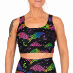 A woman wearing a matching black activewear set with a vibrant neon rainbow bat print, featuring a sports bra and high-waisted leggings against a plain white background.