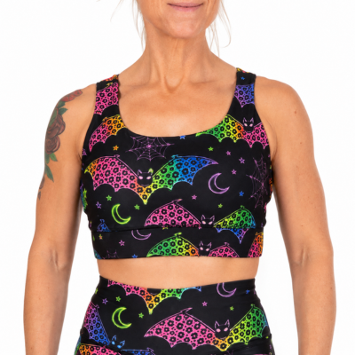 A woman wearing a matching black activewear set with a vibrant neon rainbow bat print, featuring a sports bra and high-waisted leggings against a plain white background.