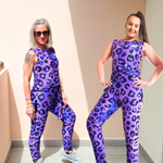 Two women wearing purple leopard print outfits posing against a beige wall.