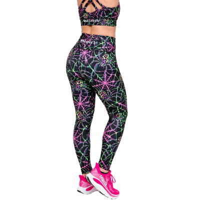 A model wearing a matching activewear set featuring a black sports bra and high-waisted leggings with a vibrant neon spiderweb pattern in pink, green, and blue, paired with pink trainers.