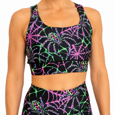 A cropped view of a person wearing a black sports bra and matching high-waisted bottoms with a neon spiderweb print in pink, green, and blue on a white background.