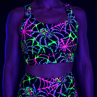 A black two-piece activewear set featuring a vibrant neon UV-reactive spiderweb and spider print, shown on a model under blacklight.